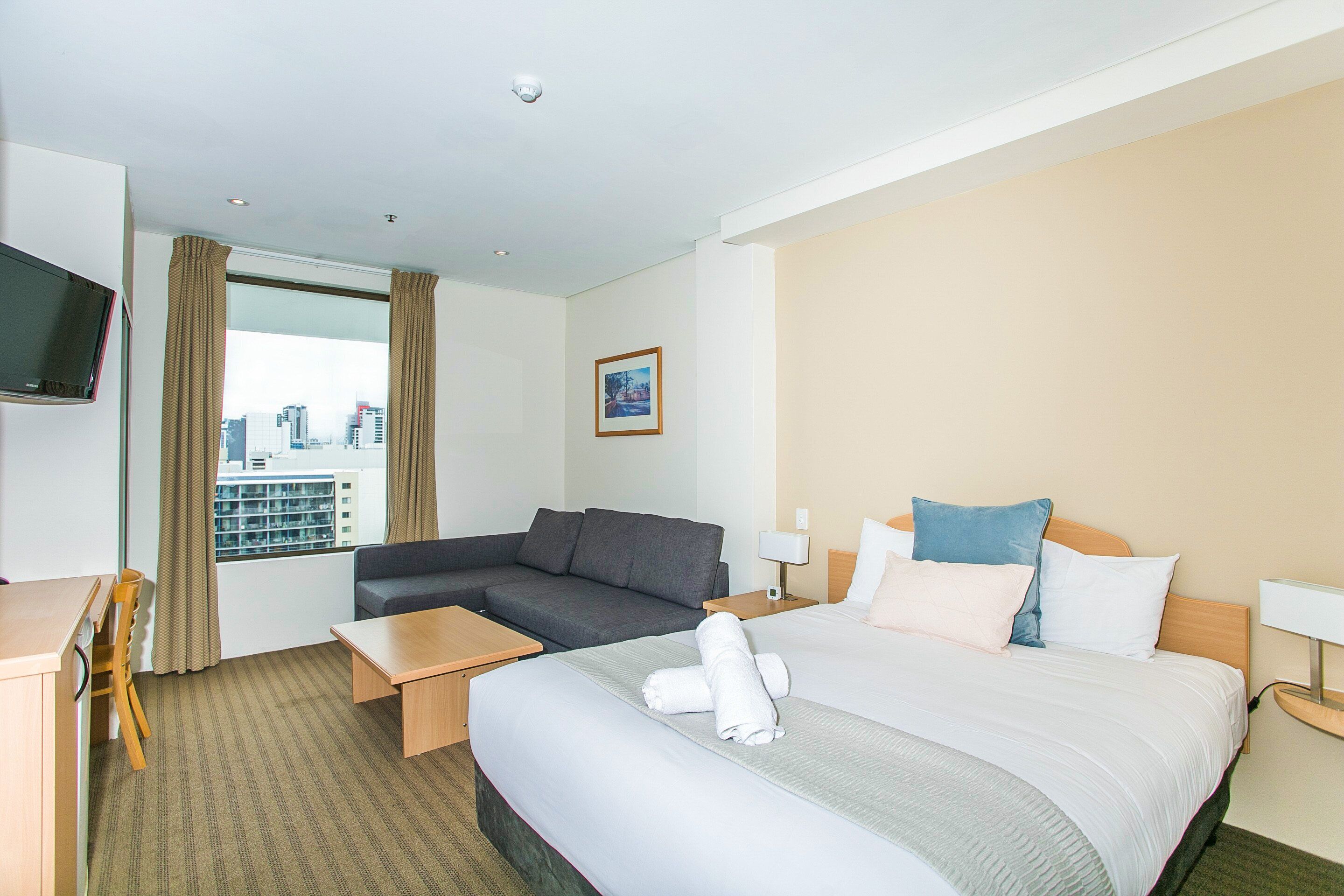 A hotel room with a bed, a sofa, a desk, and a television.
