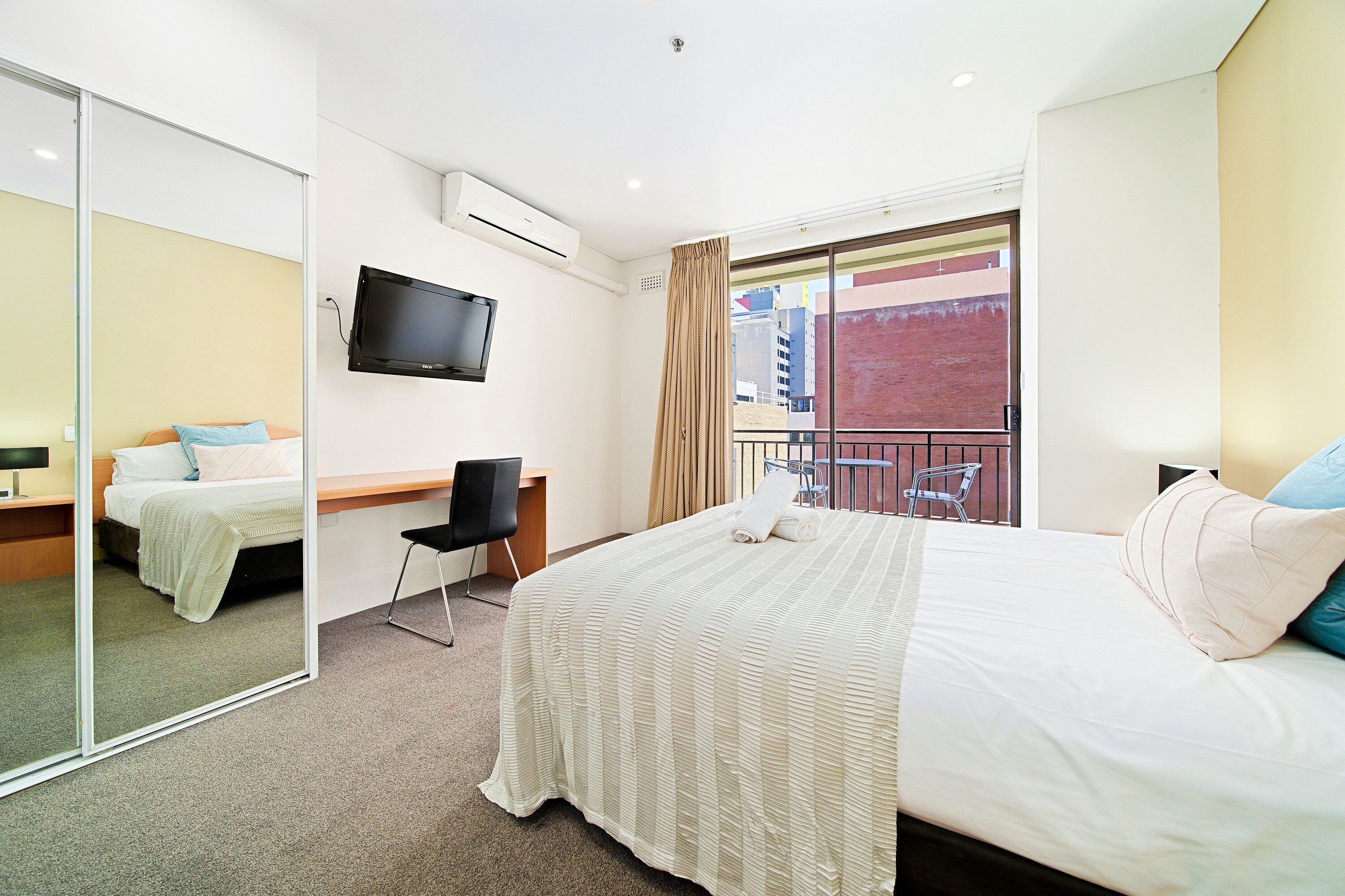 Une chambre d’hôtel comprenant un lit, un bureau, une chaise, une télévision et un balcon avec vue sur les bâtiments.