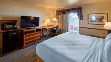 A hotel room with a bed, a desk with a computer, a television, a microwave, and a refrigerator.