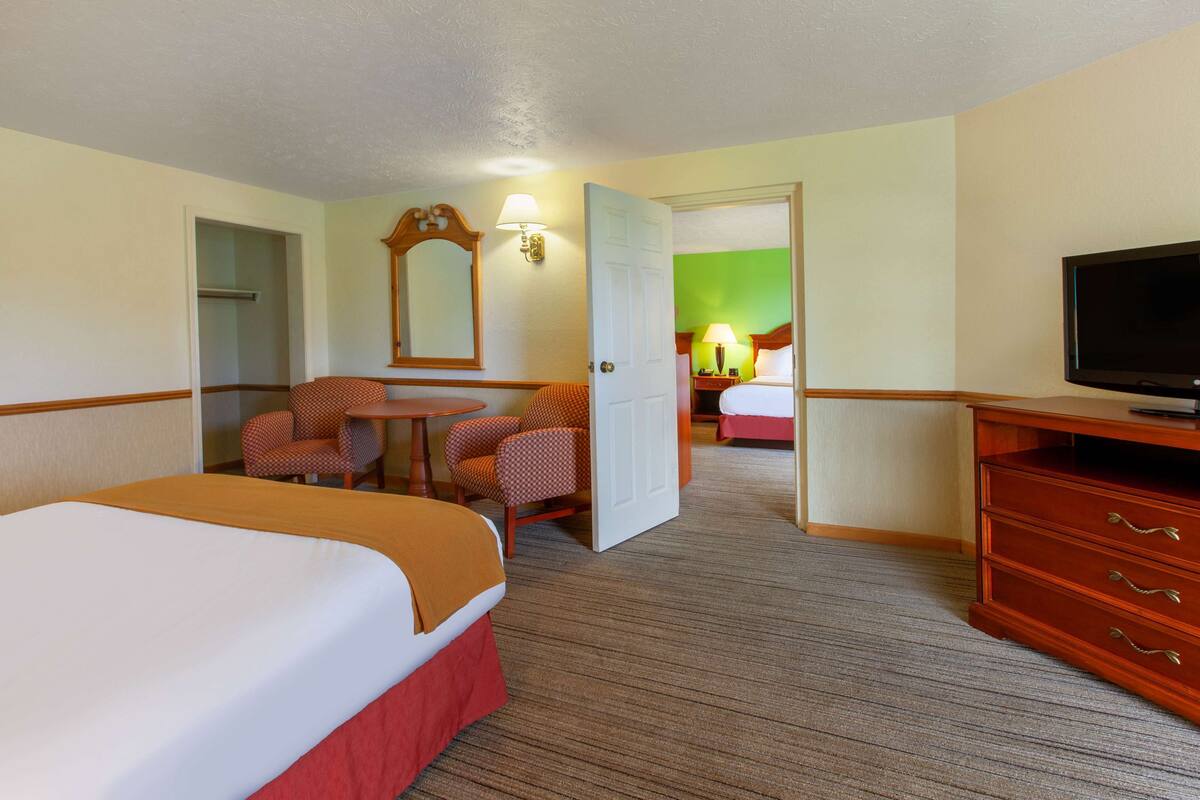 A hotel room with a large bed, a desk with a chair, a television, and a wardrobe.