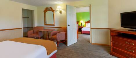 A hotel room with a large bed, a desk with a chair, a television, and a wardrobe.
