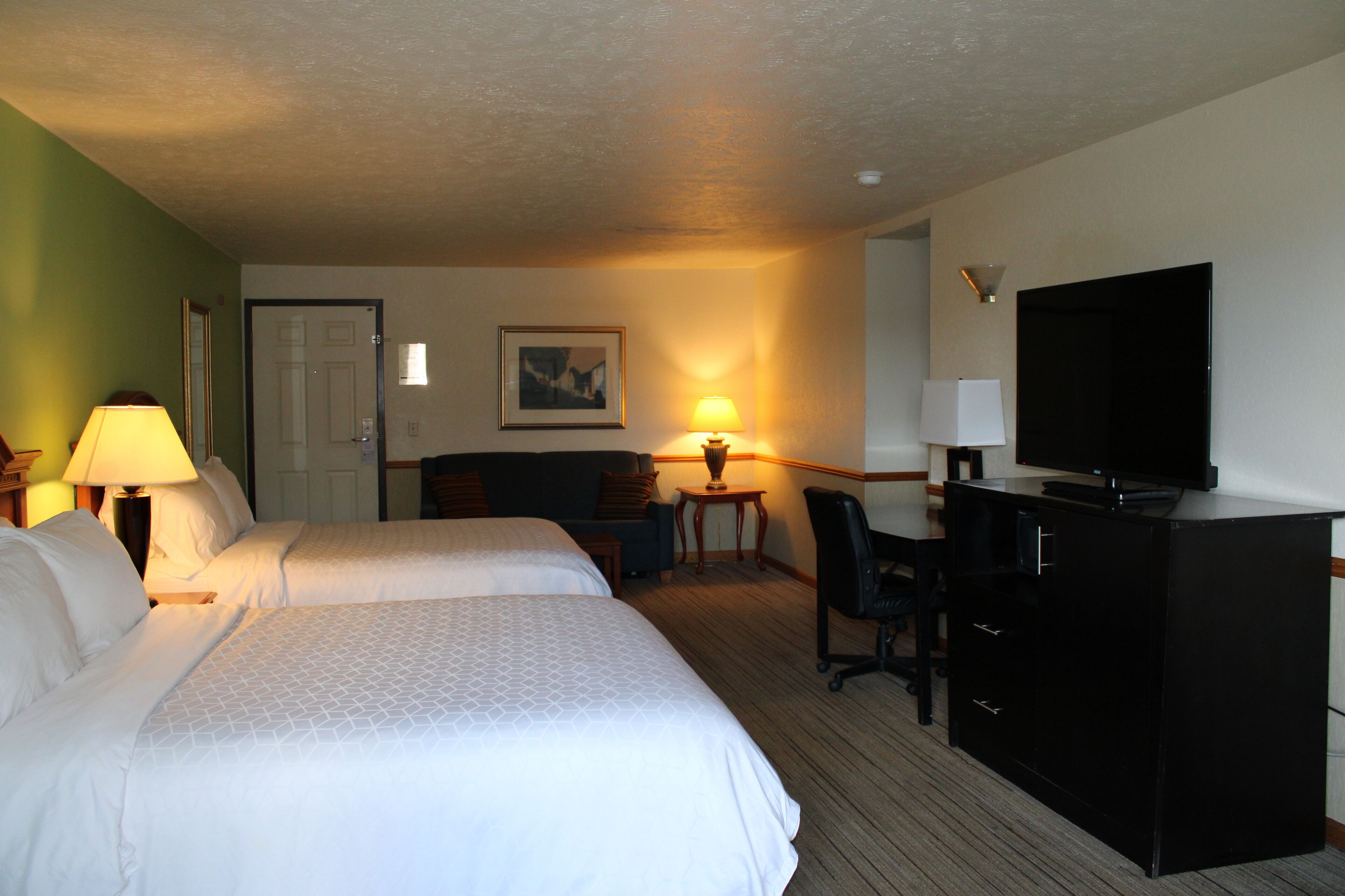 A hotel room with two beds, a desk with a chair, a television, and a lamp.