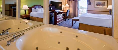Quarto de hotel com uma banheira grande, uma cama, uma escrivaninha com televisão e vista para o exterior.