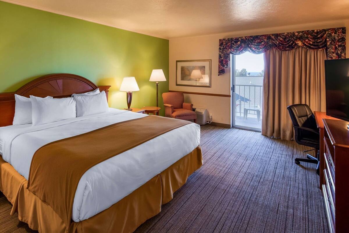 A hotel room with a large bed, two bedside lamps, a chair, a desk, and a television.