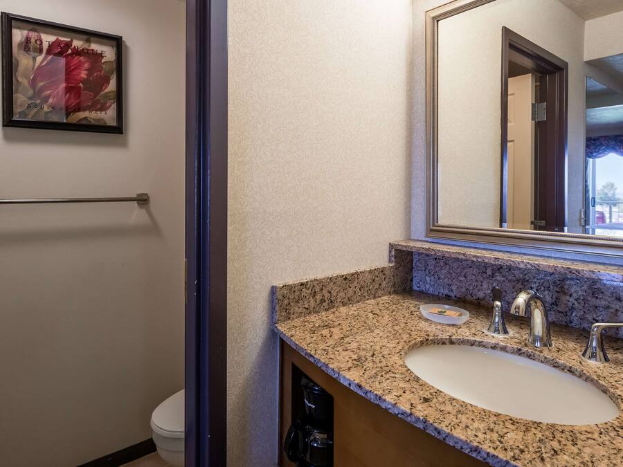 Un bagno con lavabo su piano in granito, uno specchio grande e un'opera d'arte incorniciata a parete.