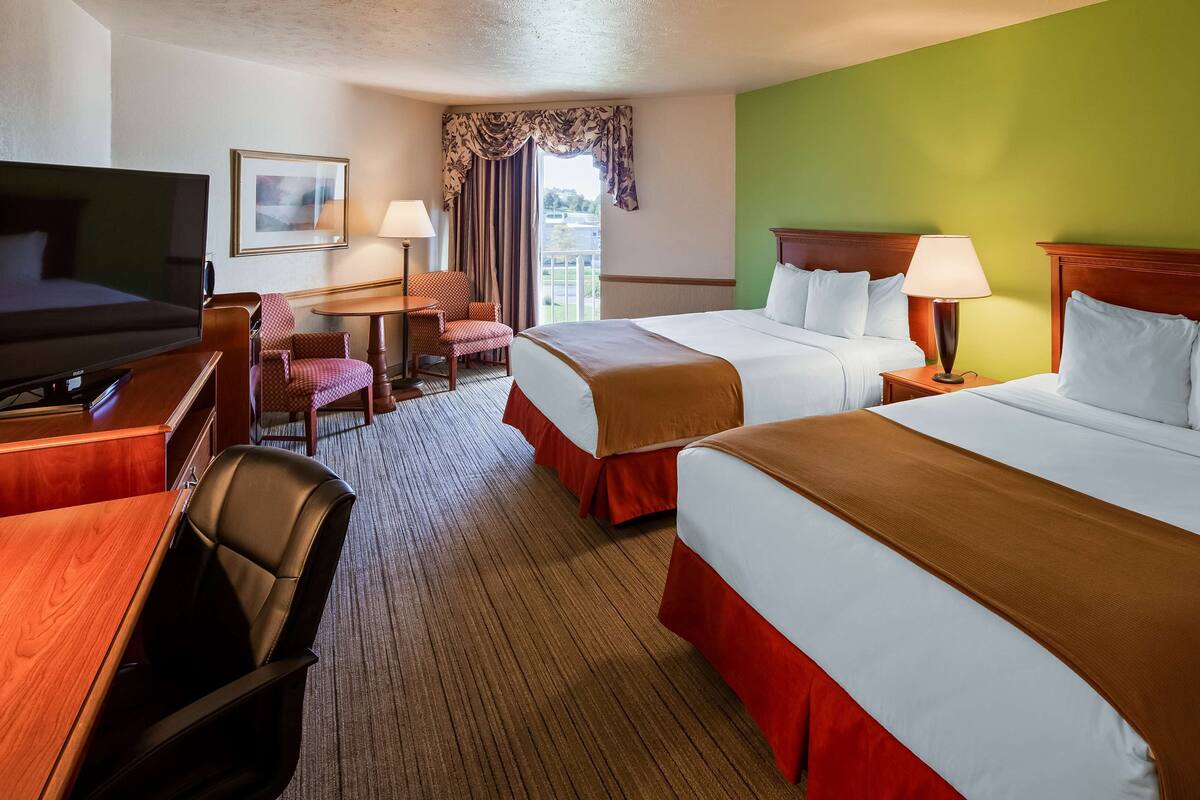 A hotel room with two beds, a desk with a TV, a chair, and a window with curtains.