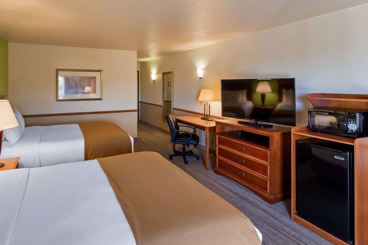 A hotel room with two beds, a desk with a TV, a microwave, and a refrigerator.