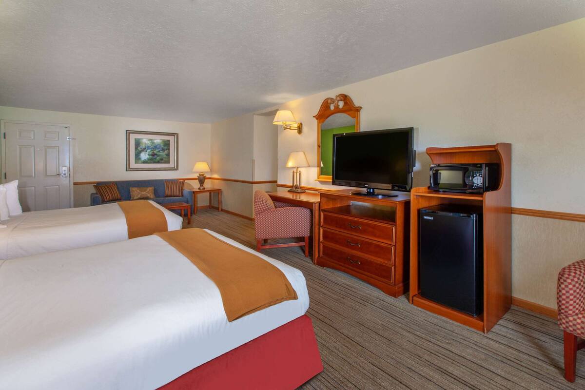 A hotel room with two beds, a desk with a television, a microwave, and a refrigerator.