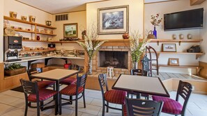 A cozy living room with a fireplace, a coffee station, and a dining area with red upholstered chairs.