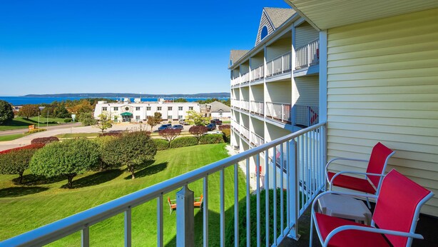 A multi-story building with a balcony, a lawn, and a view of the sea. - Apple Tree Inn, SureStay Collection by Best Western (Petoskey)