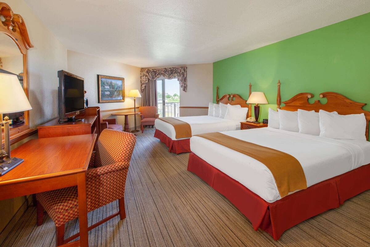 A hotel room with two beds, a desk with a chair, a television, and a window with a view.