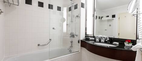 A modern bathroom with a glass-enclosed shower, a white bathtub, a dark-toned vanity, and a large mirror.