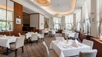 Ein geräumiges Restaurant mit mehreren Tischen und Stühlen, großen Fenstern mit Vorhängen sowie einem gestreiften Boden.