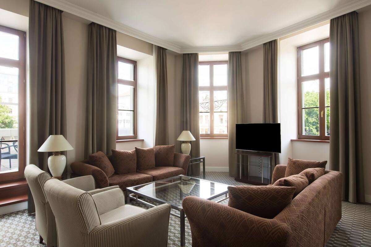 A hotel room with a large window, a flat-screen TV, and a sofa set.