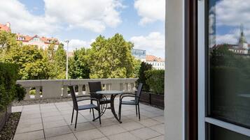 An outdoor patio with a table and chairs, a railing, and a view of buildings and trees.