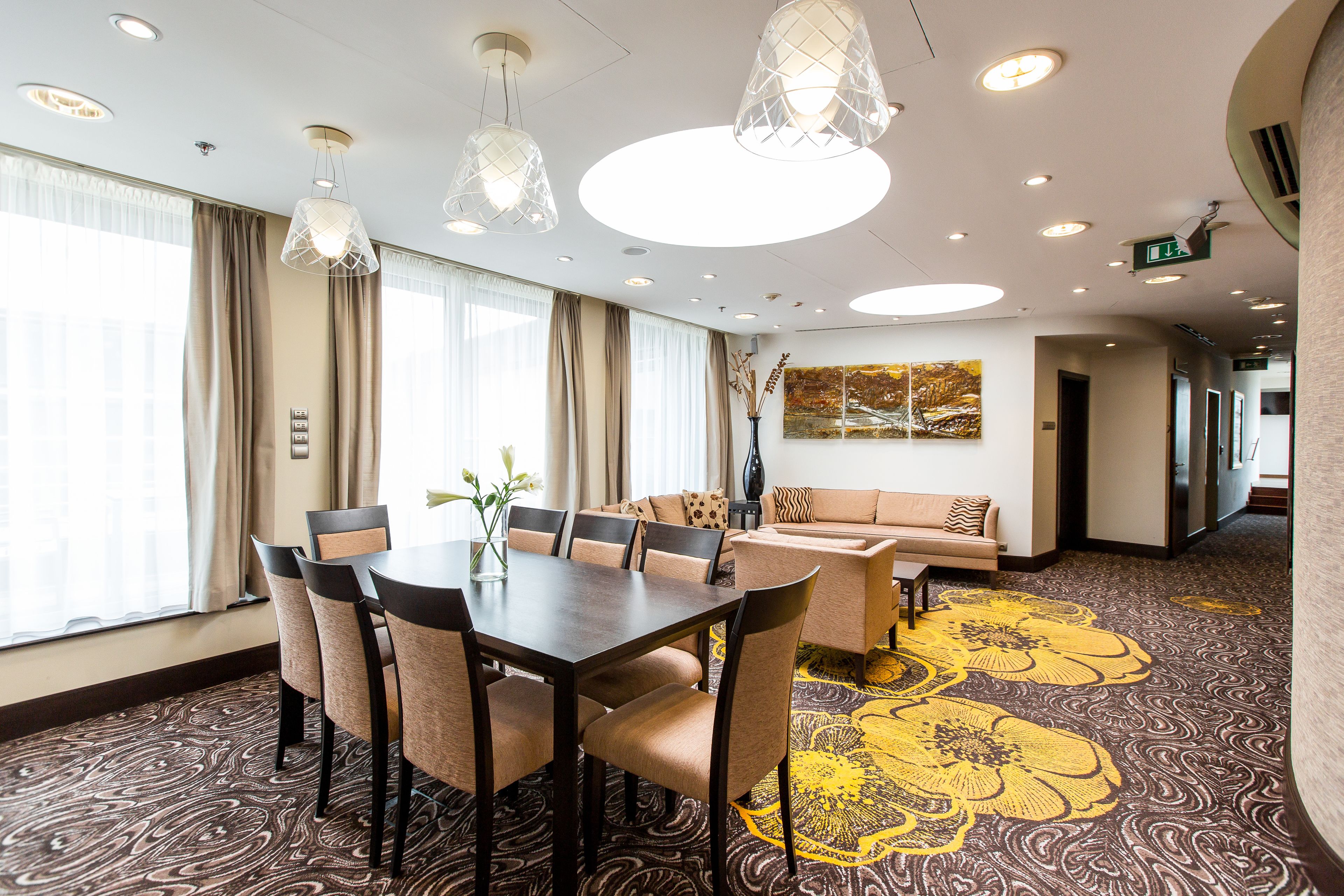 Habitación de hotel con comedor, sofá y un amplio ventanal con cortinas.