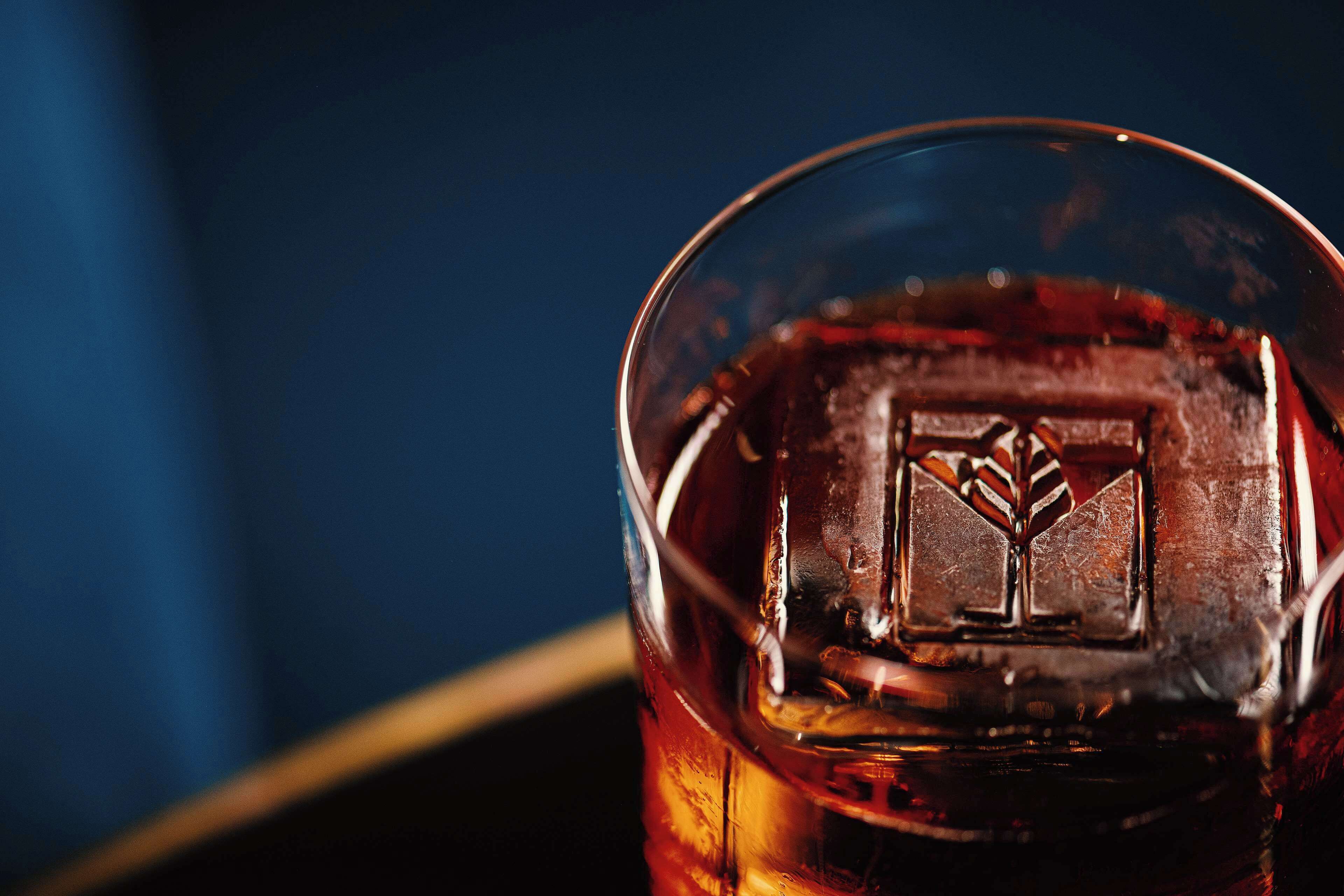 A close-up of a glass with a clear liquid and an ice cube.