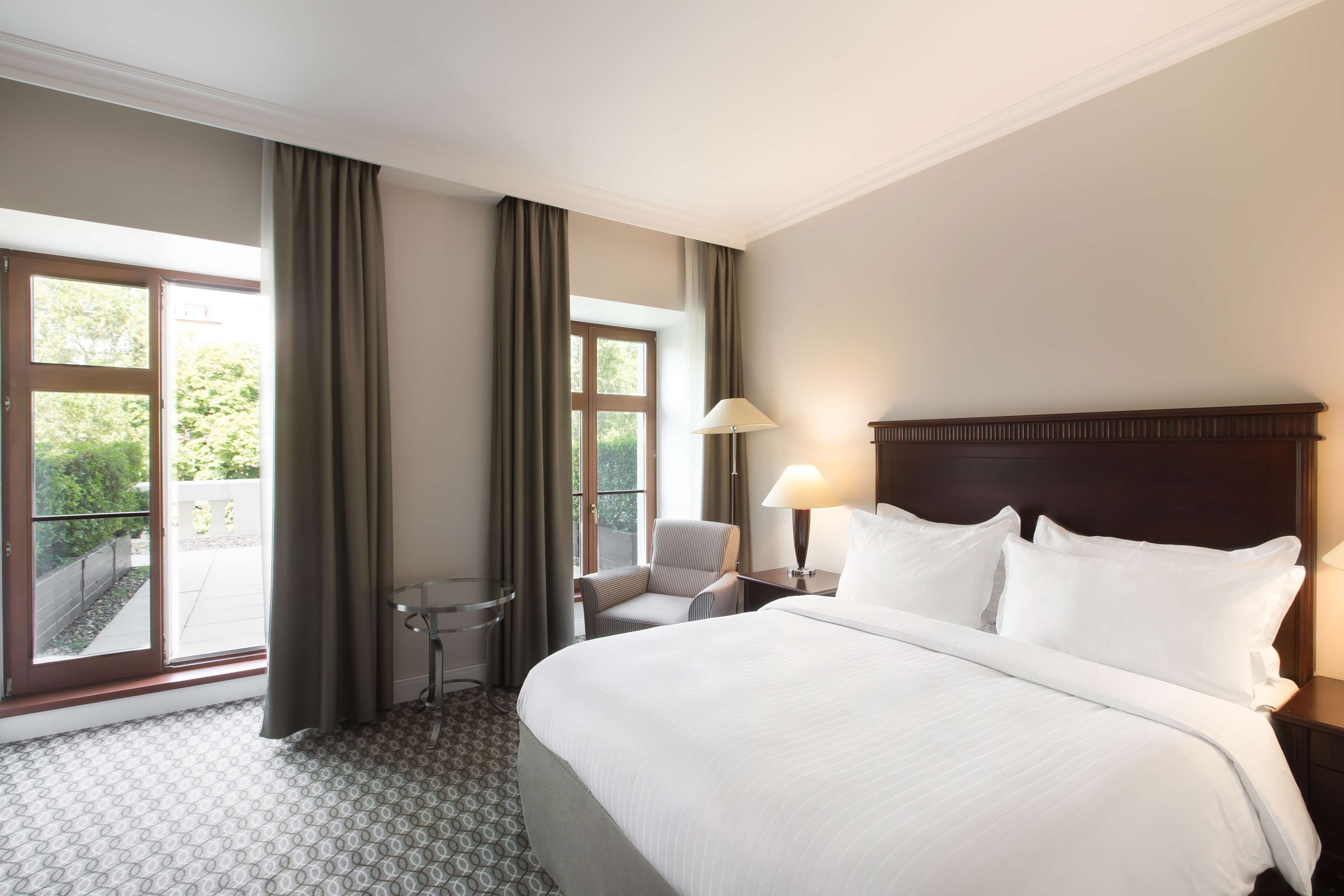 A hotel room with a large bed, a chair, a table, and a lamp.