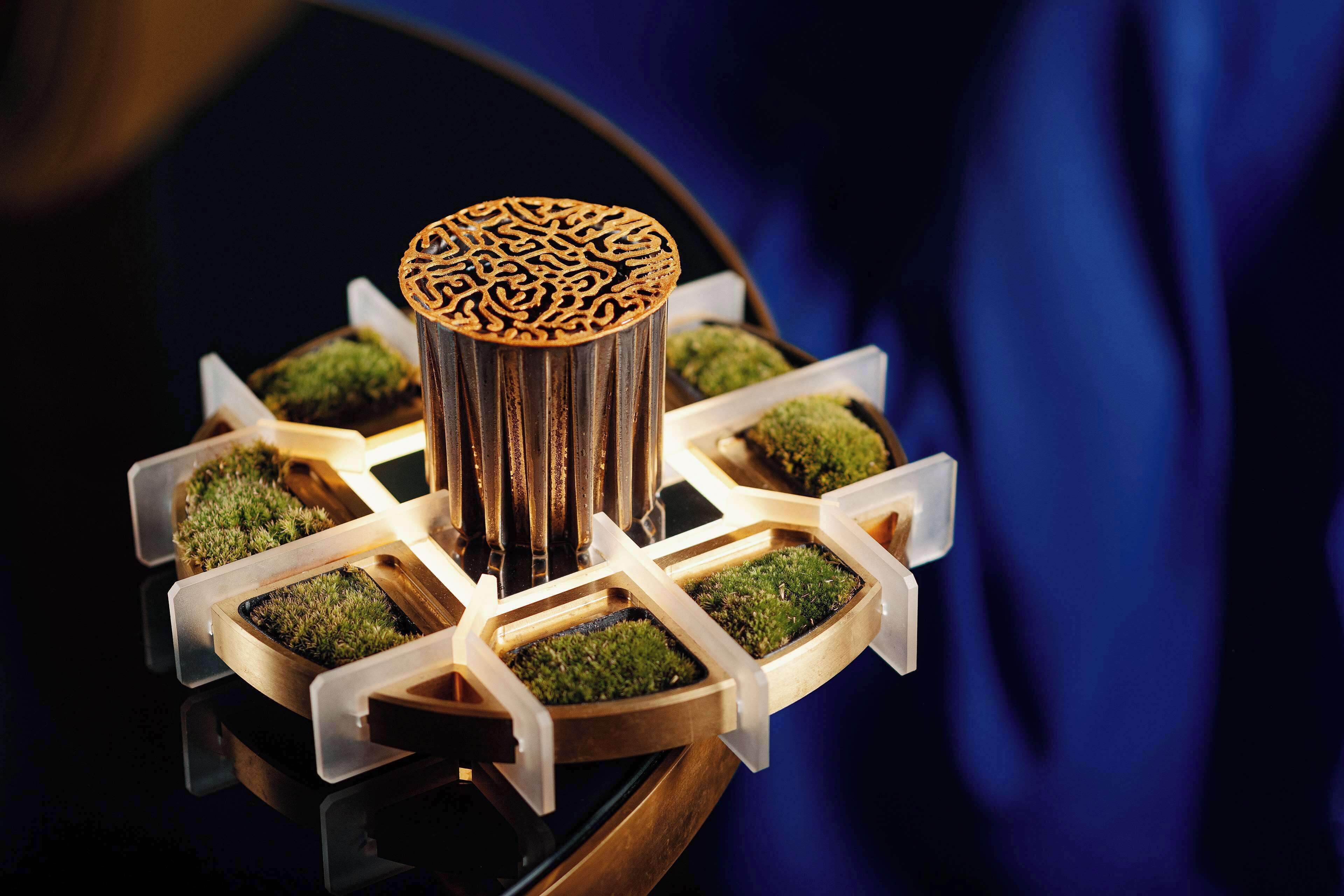 Een decoratieve houten standaard met een patroon bovenop en meerdere vakken gevuld met groen mos.