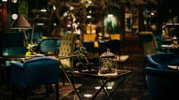 A dimly lit interior with blue upholstered chairs, a glass-top table with a plant, and a green plant in a pot.