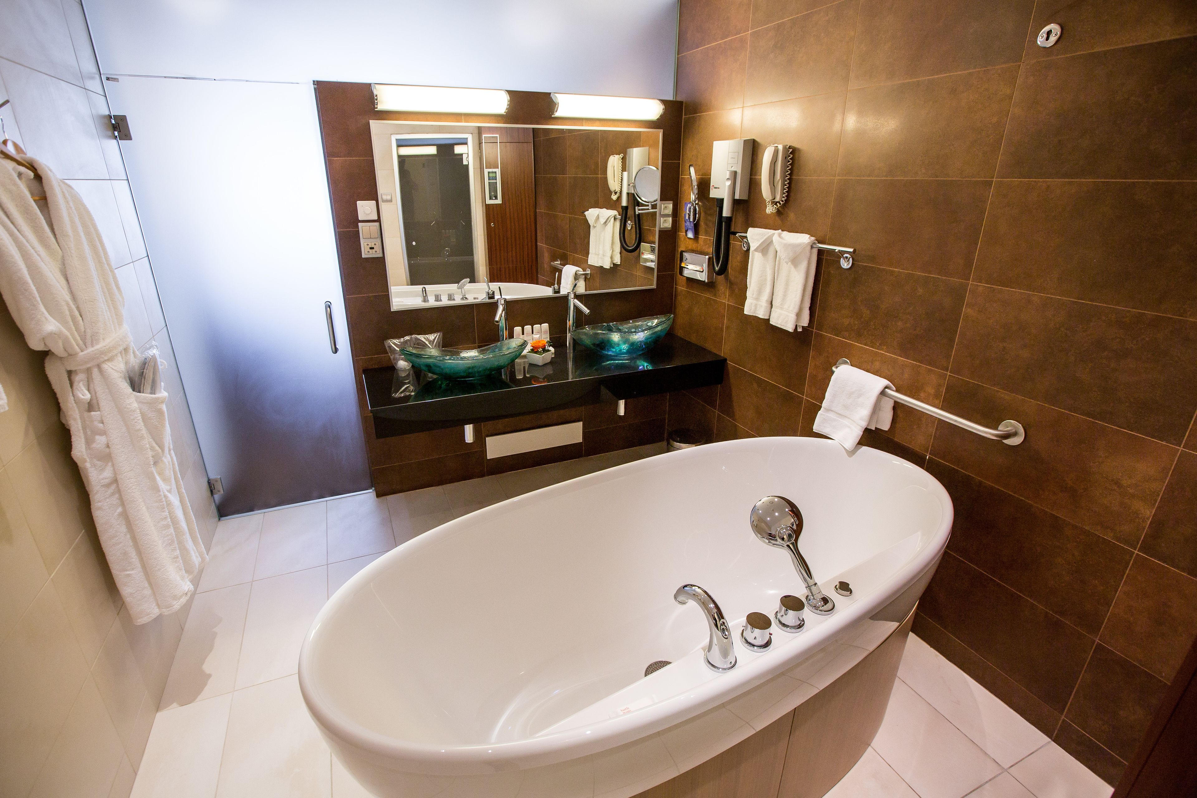 Un baño moderno con una bañera independiente, un lavabo de vidrio y un espejo grande.