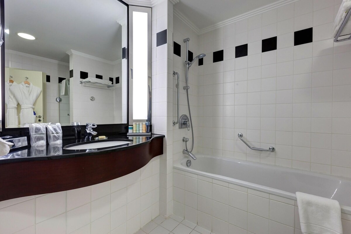 Un baño moderno con ducha de azulejos blancos, una bañera y un lavamanos con encimera oscura.