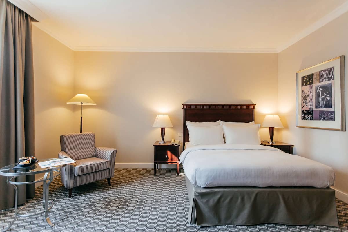 A hotel room with a bed, two bedside tables with lamps, a chair, and a small table with a menu.