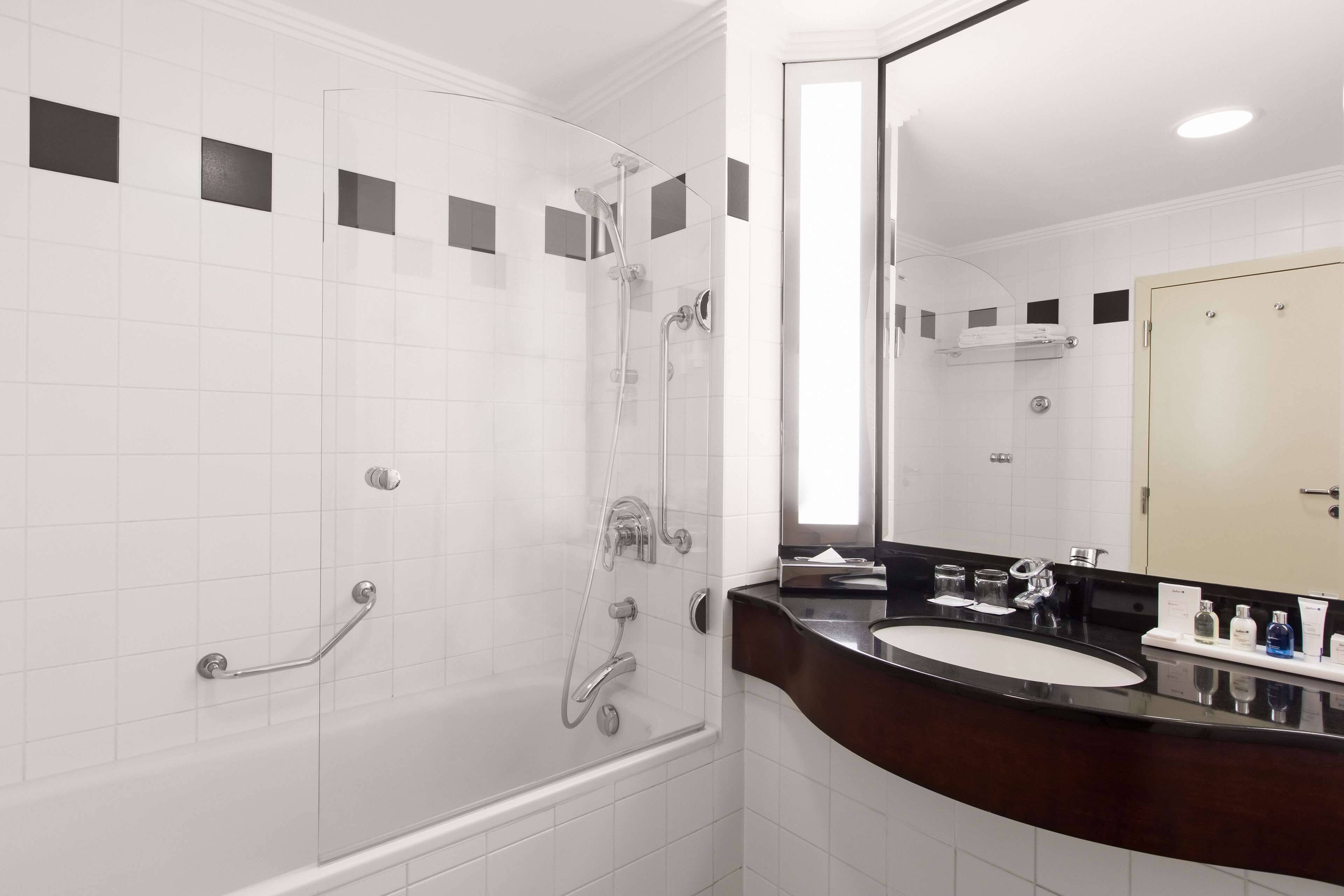 Un baño moderno con ducha envuelta en vidrio, tocador con encimera oscura y un espejo grande.