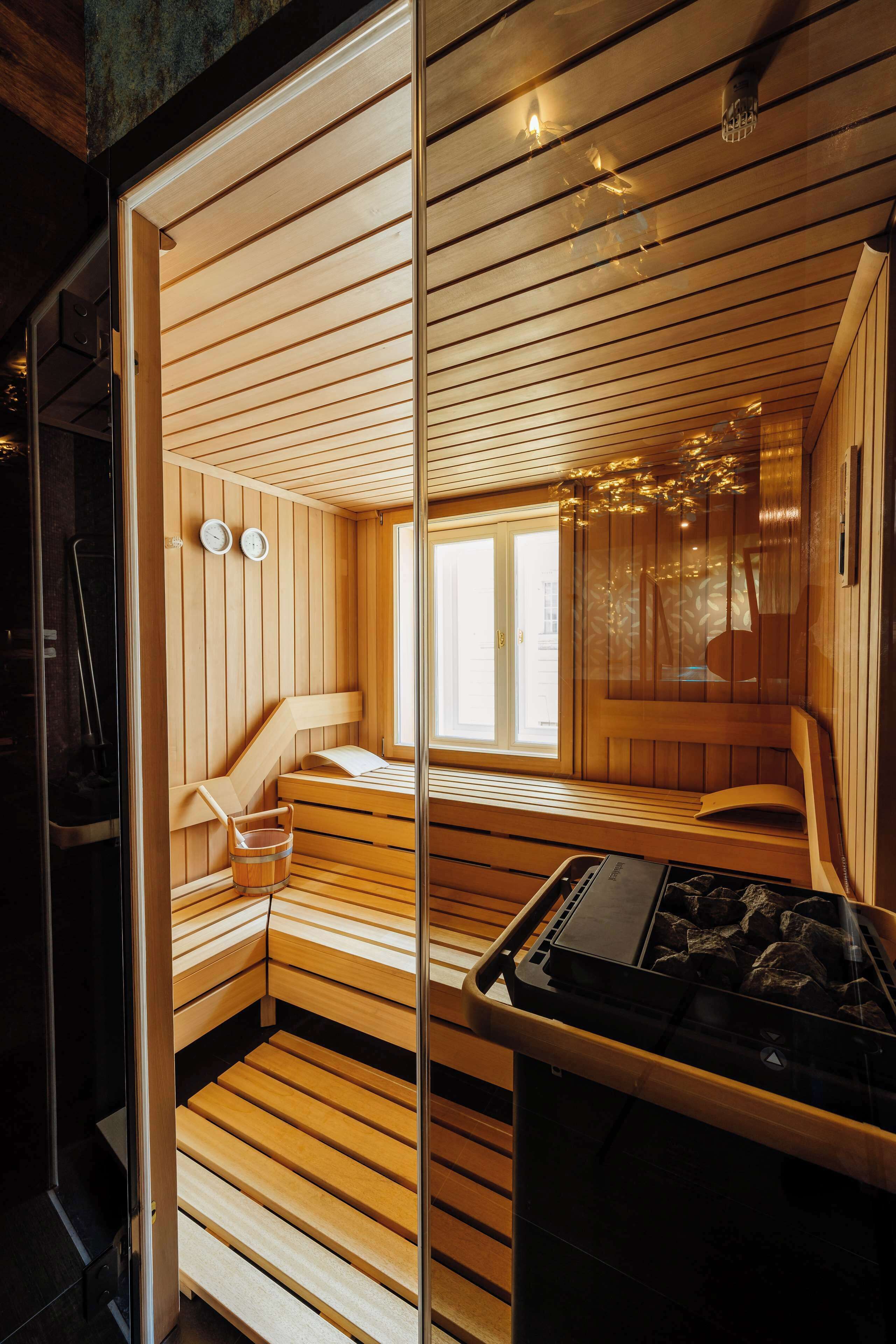 Sauna, jossa on puiset lauteet, lasiovi ja näkyvissä oleva saunatila, jossa on ikkuna.