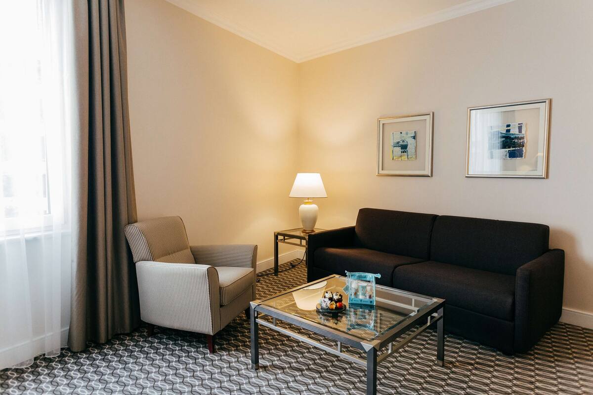 A hotel room with a sofa, armchair, and a glass coffee table.