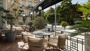 An outdoor seating area with wicker furniture, a round table, and potted plants. - Radisson Blu Carlton Hotel, Bratislava (Bratislava)