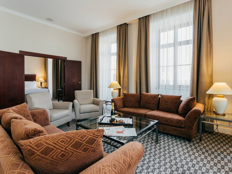 Quarto de hotel com sofá, poltrona e mesa de centro de vidro.