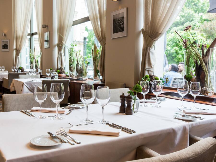 A dining area with tables set for a meal, featuring white tablecloths, glassware, and neatly arranged cutlery.