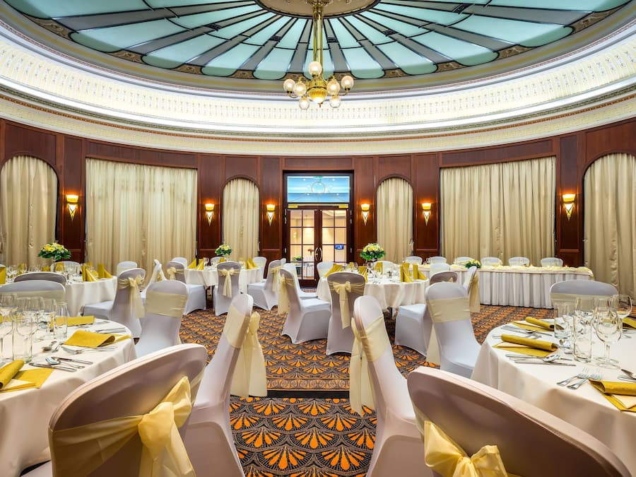 A banquet hall with round tables, white chairs, and chandeliers.