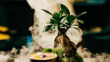 A small bonsai tree on a moss-covered base with a bowl and a flower.