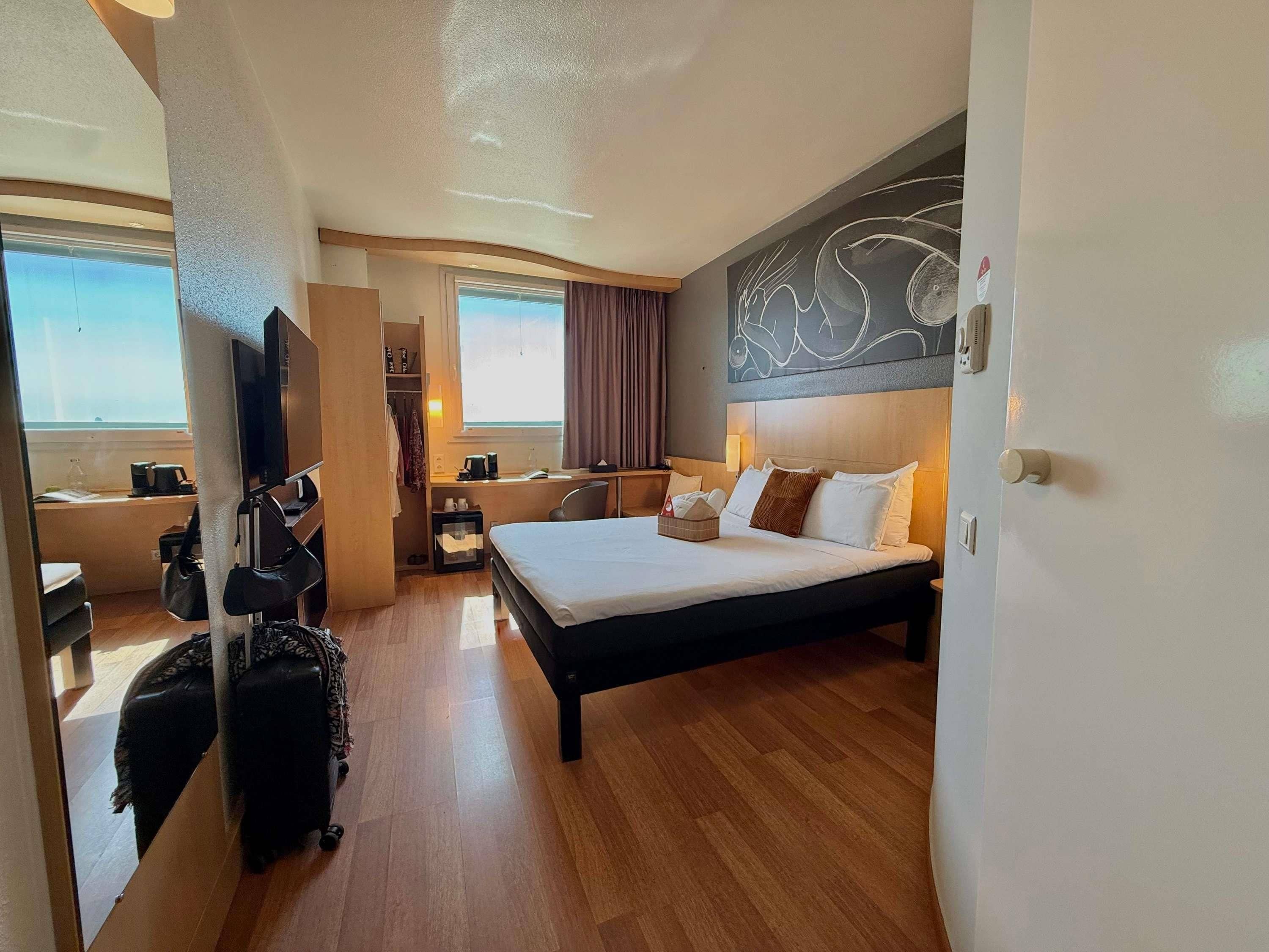 Una habitación de hotel con cama, escritorio, televisor, armario y vistas al exterior.