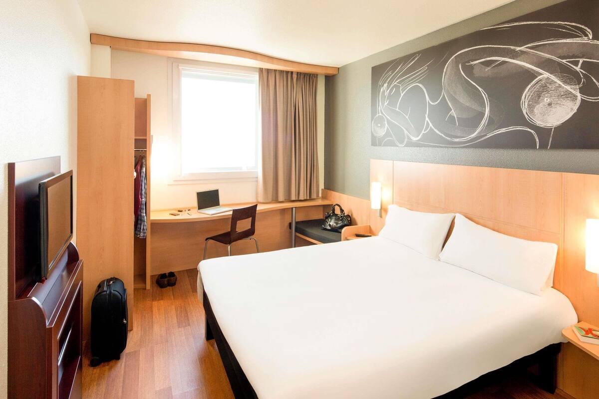 Habitación de hotel con una cama grande, un escritorio con computadora, una silla y televisión.