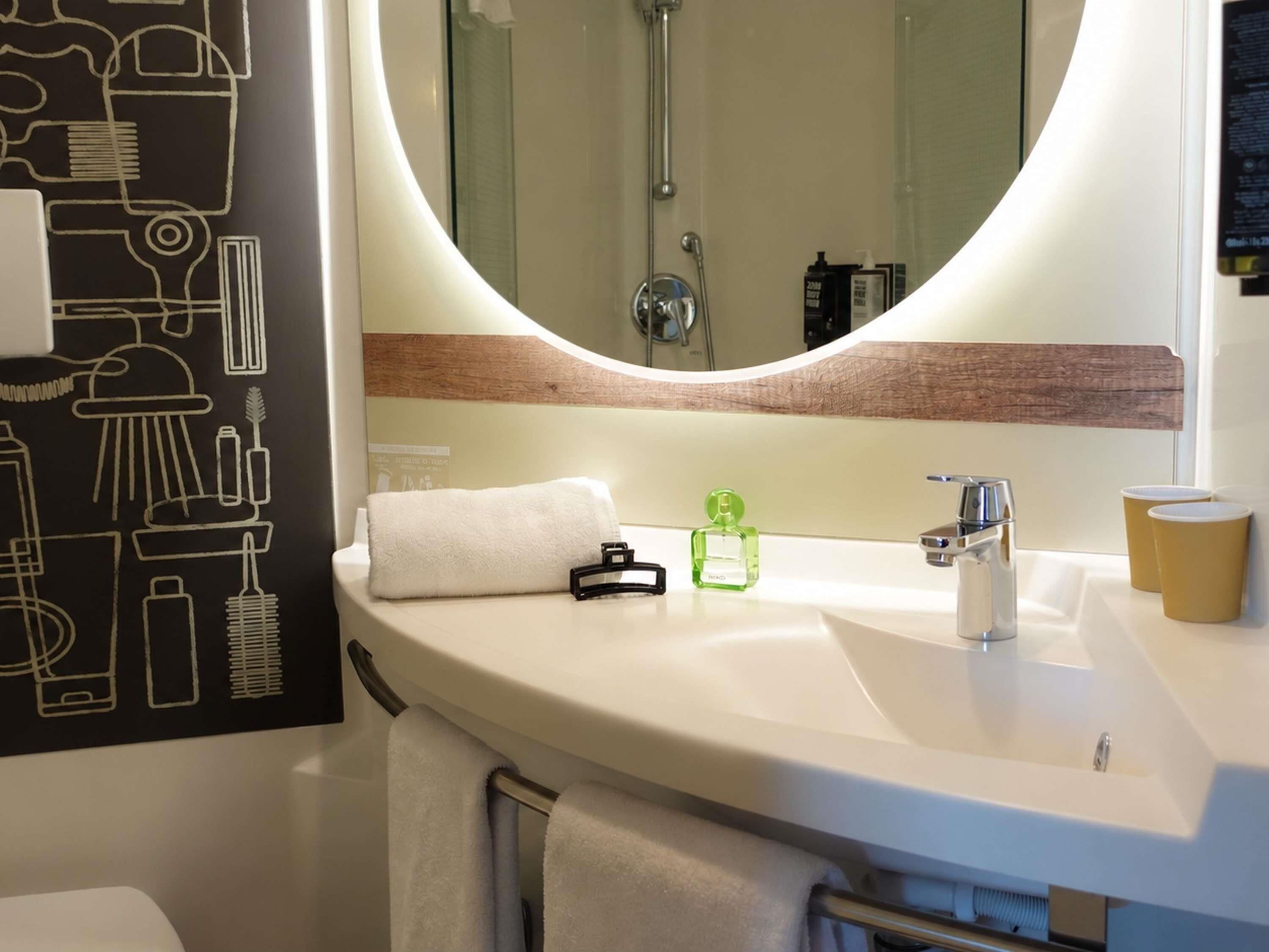 Un baño con lavamanos blanco, un espejo, toallero y ducha.