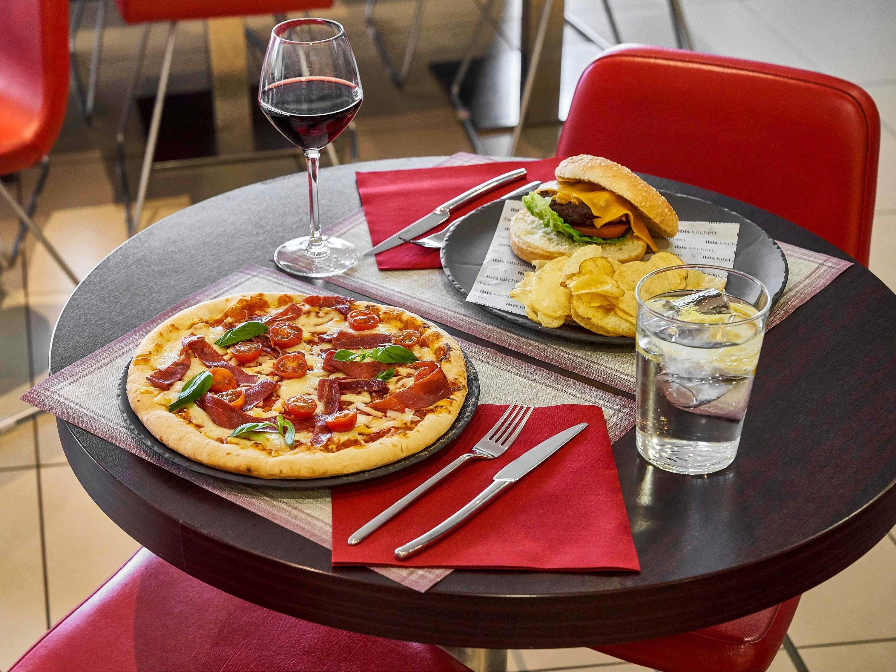 Un tavolo con pizza, hamburger, patatine, un bicchiere d'acqua e posate.