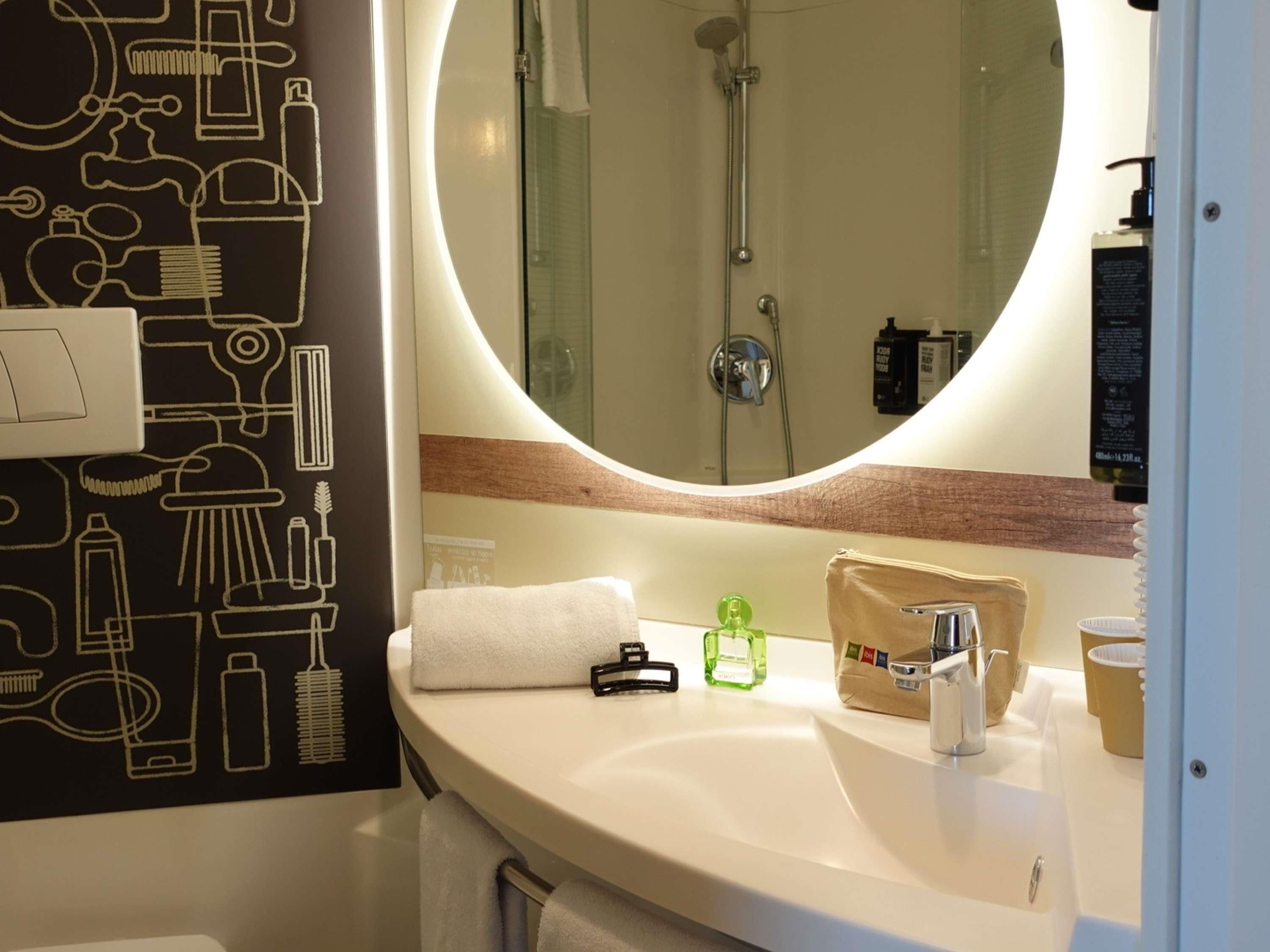 A bathroom with a round mirror, a sink, and a shower.