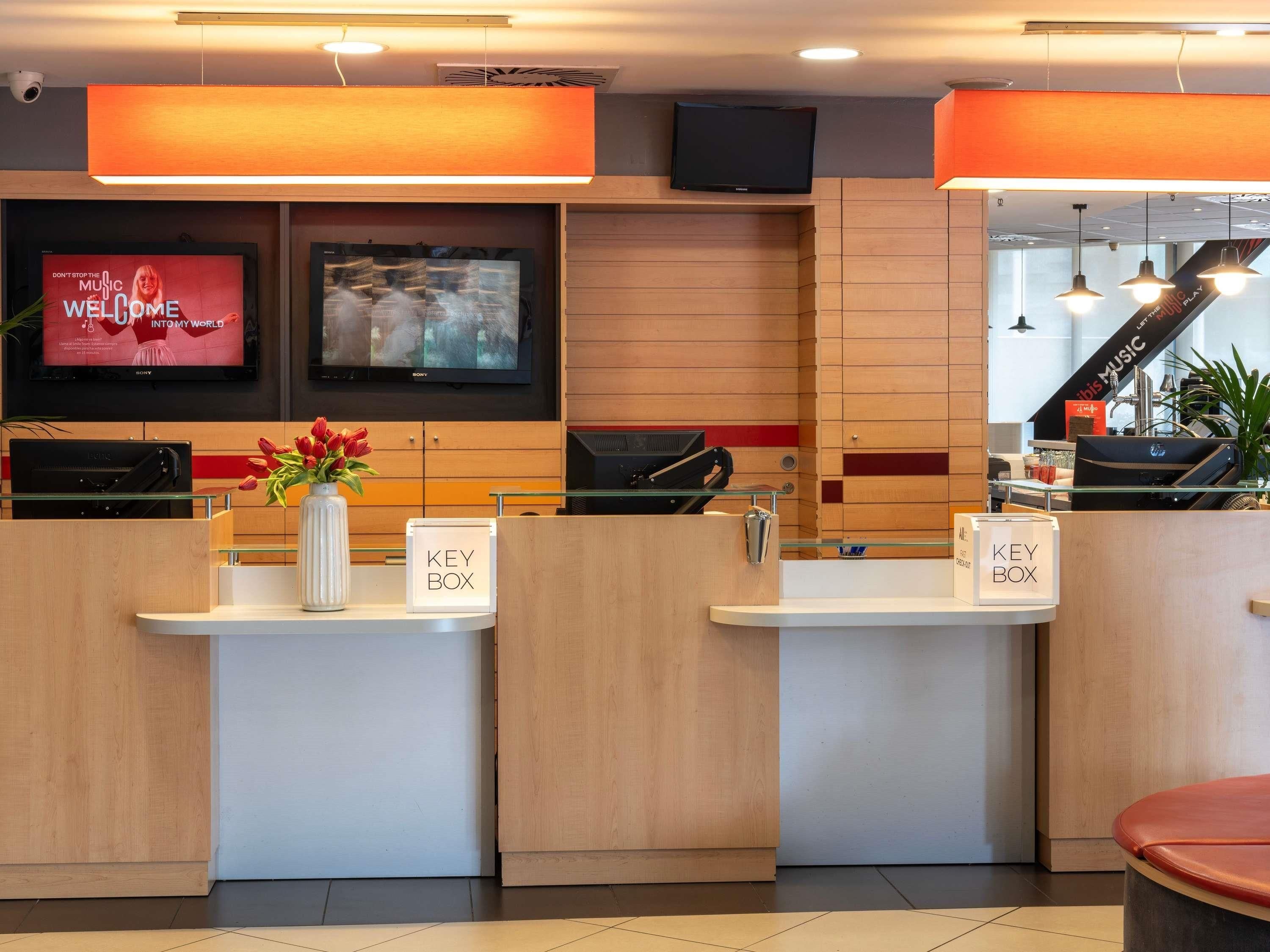 A hotel reception area with wooden paneling, a Sony TV displaying a movie poster, a key box, and a reception desk.