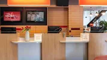 A hotel reception area with wooden paneling, a Sony TV displaying a movie poster, a key box, and a reception desk.
