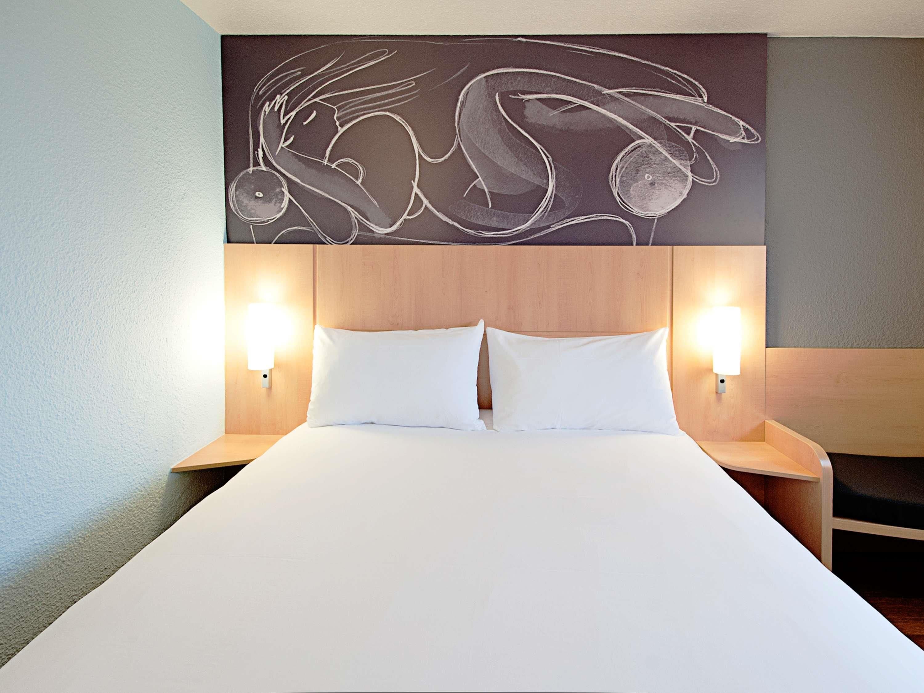 Een hotelkamer met een groot bed, twee nachtkastjes en een kunstwerk aan de muur.