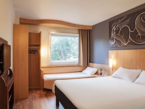 Une chambre d’hôtel comprenant un lit, un coin salon avec une fenêtre, une télévision et un porte-manteau.