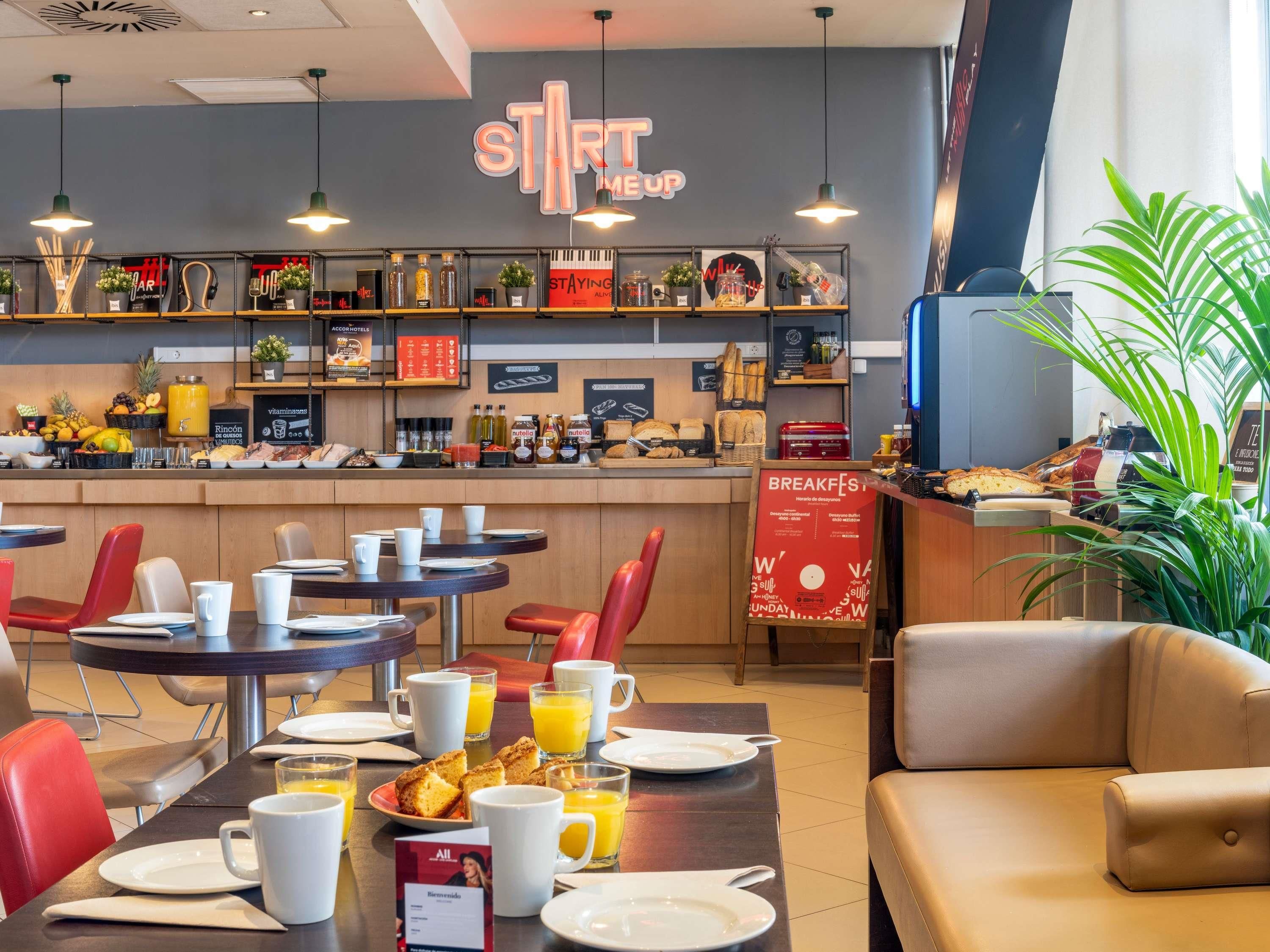 Een ontbijtruimte met tafels, stoelen en een toonbank met eten en drinken.