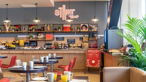 Un espace réservé au petit-déjeuner, avec des tables, des chaises et un comptoir où sont exposés les aliments et les boissons.