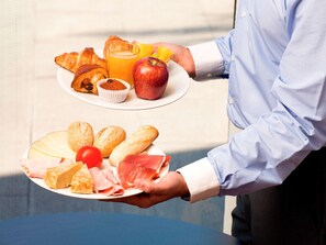 A person holding a plate with croissants, a muffin, a glass of orange juice, an apple, and a plate with cheese, ham, and bread rolls. - ibis Barcelona Meridiana (Barcelona)