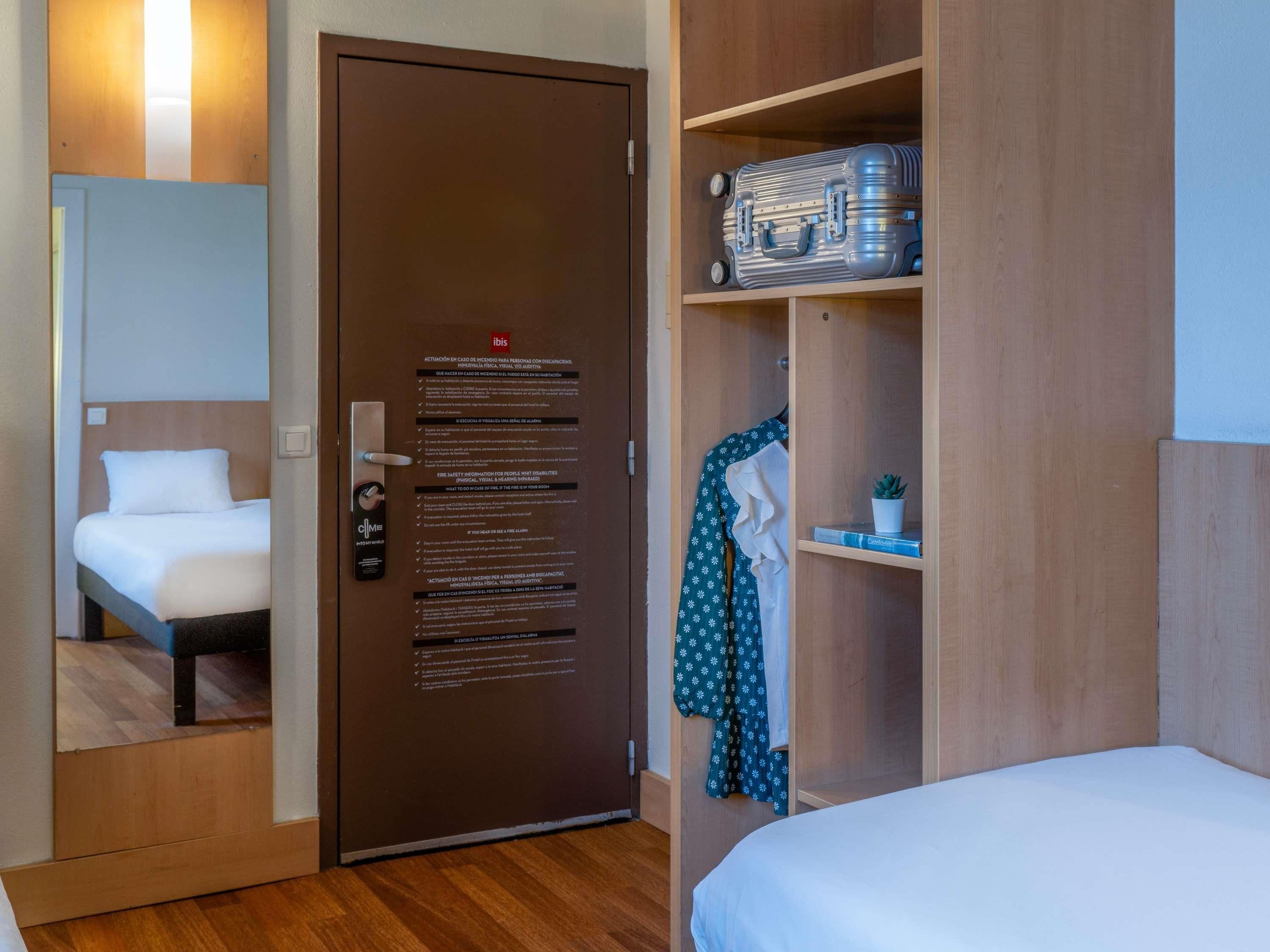 A hotel room with a bed, a wardrobe, and a door with safety instructions.