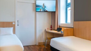 Une chambre d’hôtel avec deux lits, un bureau avec un ordinateur, un téléviseur fixé au mur et une fenêtre avec des rideaux.