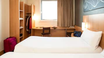 Une chambre d’hôtel équipée d’un lit, d’un bureau, d’une chaise, d’une armoire et d’une fenêtre avec des rideaux.